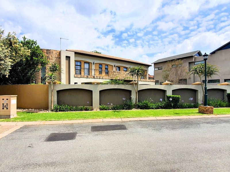Front elevation of a multi-story residential property featuring stone cladding, a balcony, and a secure boundary wall with landscaped garden beds.