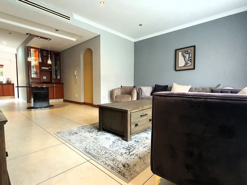 Spacious open-plan living area featuring large format floor tiles, recessed downlighting, ducted air conditioning, and a dedicated built-in bar area.