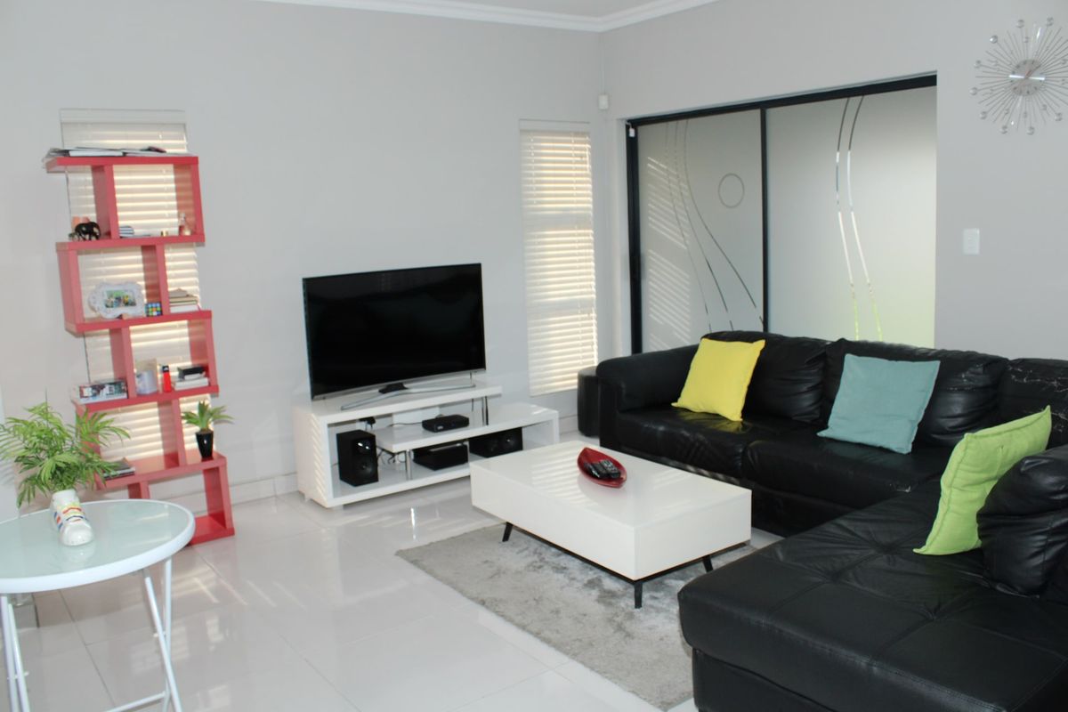 A bright living room featuring polished tiled flooring, modern sliding glass doors, and fitted venetian blinds.