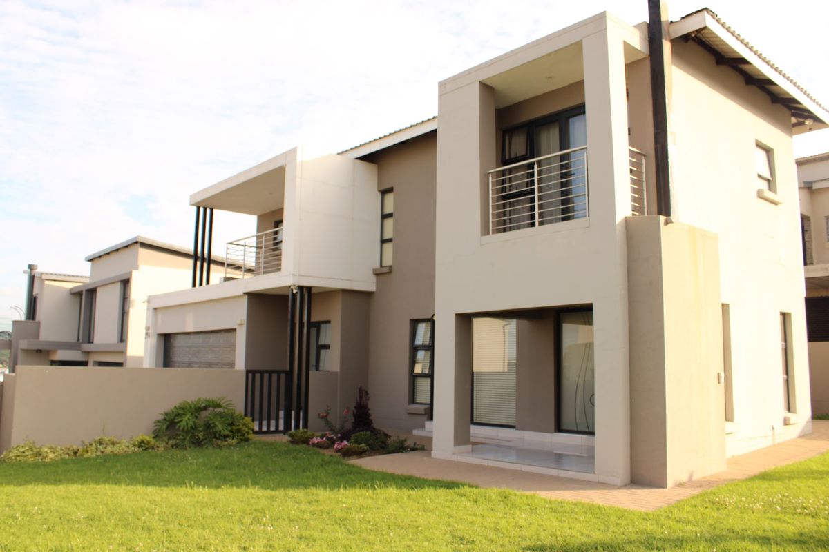 Modern double-story cluster home featuring a rear paved patio, upper-level balcony with stainless steel balustrades, and well-maintained exterior finishes.