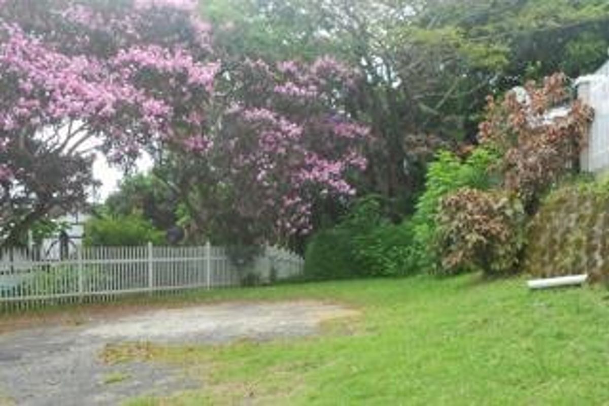 A residential garden area featuring a white picket fence, a stone retaining wall, and mature flowering trees on a sloped plot.
