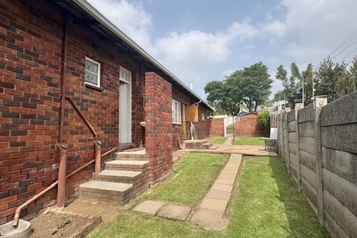 Rear exterior view of the property featuring face brick walls, a paved walkway, and a concrete boundary wall.