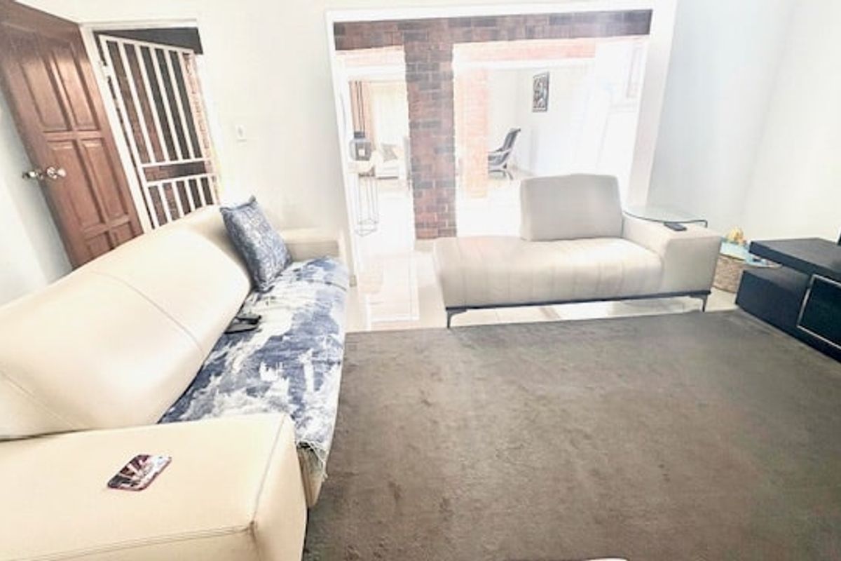 A living room featuring tiled flooring and an exposed brick architectural element, providing access to an adjacent space through a wide opening.