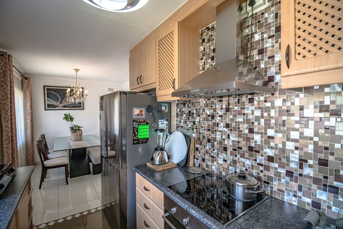 A functional kitchen featuring light wood cabinetry, granite countertops, a mosaic tile backsplash, and integrated stainless steel appliances, flowing into the dining area.