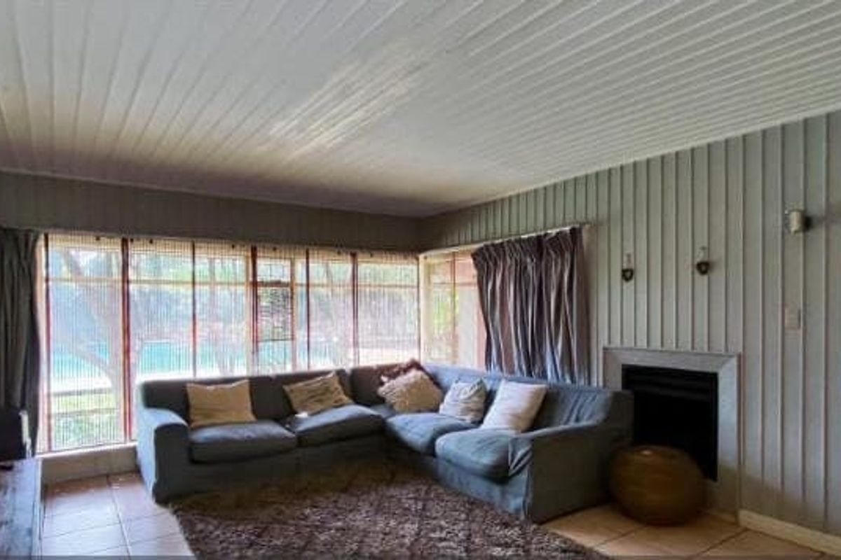 A living room featuring a fireplace, tiled flooring, and timber wall paneling, with large windows providing natural light and views of the outdoor area.