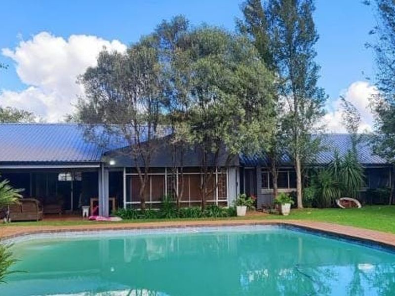 Rear view of the property featuring a swimming pool, a covered patio area, and a well-maintained garden with mature trees.