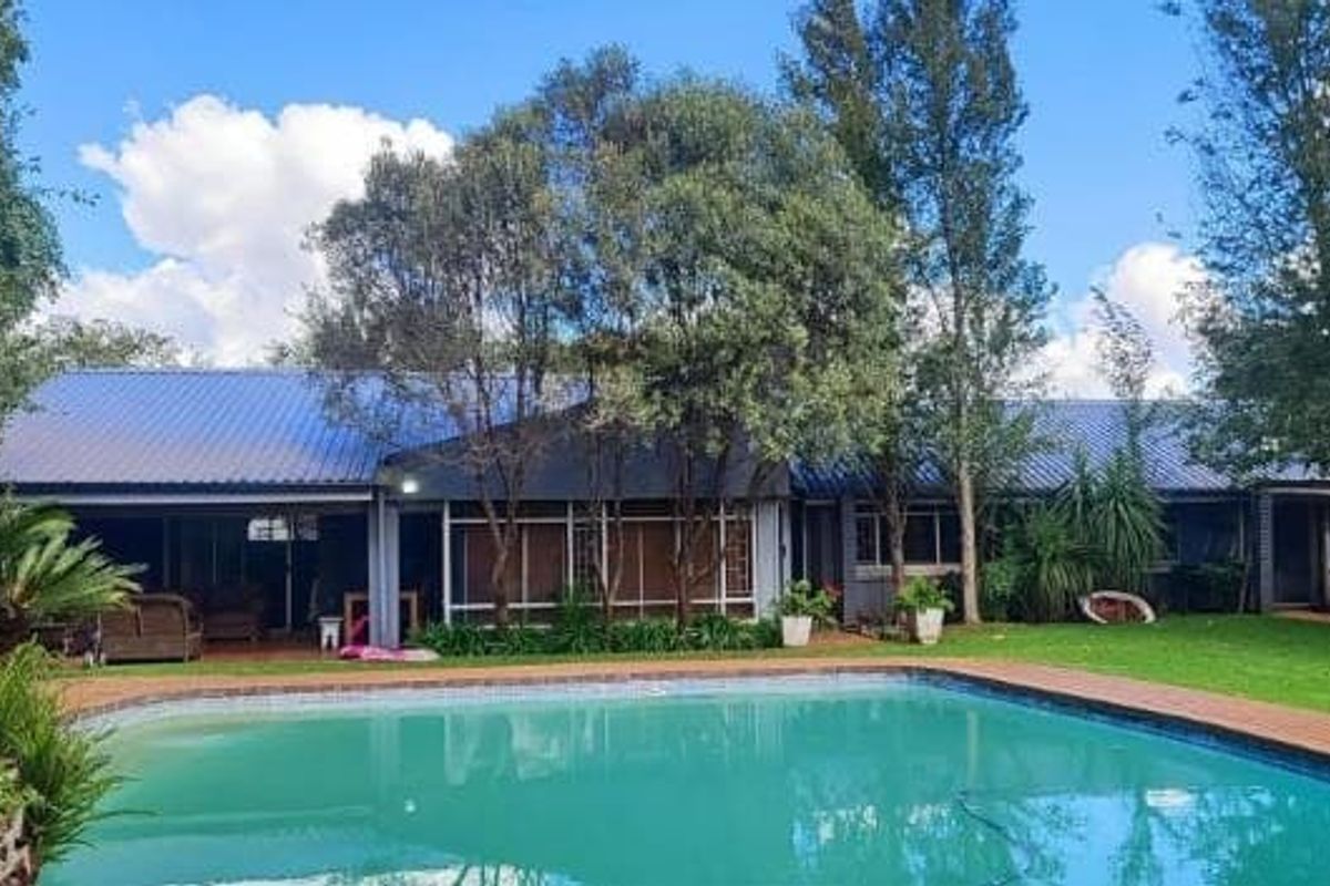 Rear view of the property featuring a swimming pool, a covered patio area, and a well-maintained garden with mature trees.