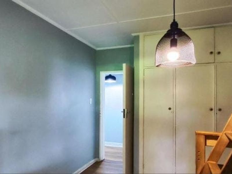 A bedroom featuring built-in cupboards, a pendant light fixture, and a tiled ceiling, with a view into an adjacent hallway.