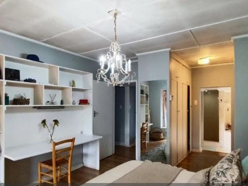 Bedroom featuring built-in desk and shelving unit, ample cupboard storage, and a central chandelier. The space offers functional layout with direct access to adjacent rooms.
