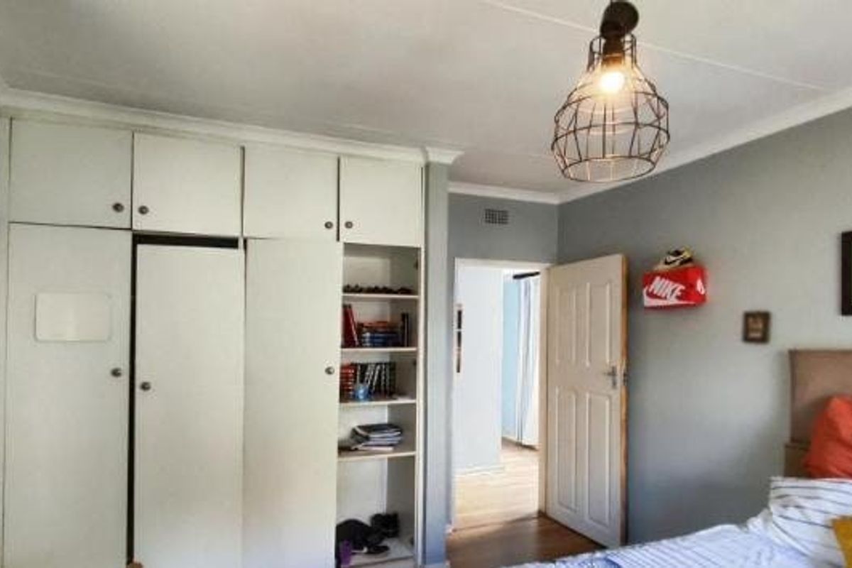 A bedroom featuring built-in floor-to-ceiling cupboards with integrated shelving and a classic panelled internal door.