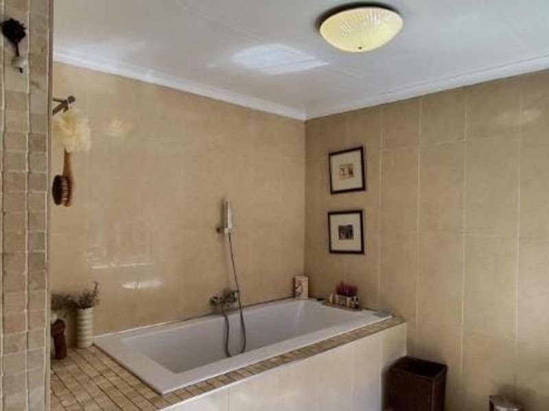 A functional bathroom featuring a built-in bathtub with a handheld shower mixer, finished with neutral ceramic wall tiles and decorative mosaic accents.