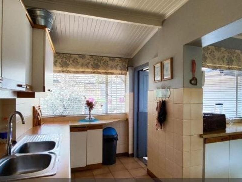 A functional kitchen featuring double bowl stainless steel sink, laminate countertops, tiled splashbacks, and ample built-in cabinetry with a classic tongue and groove ceiling.