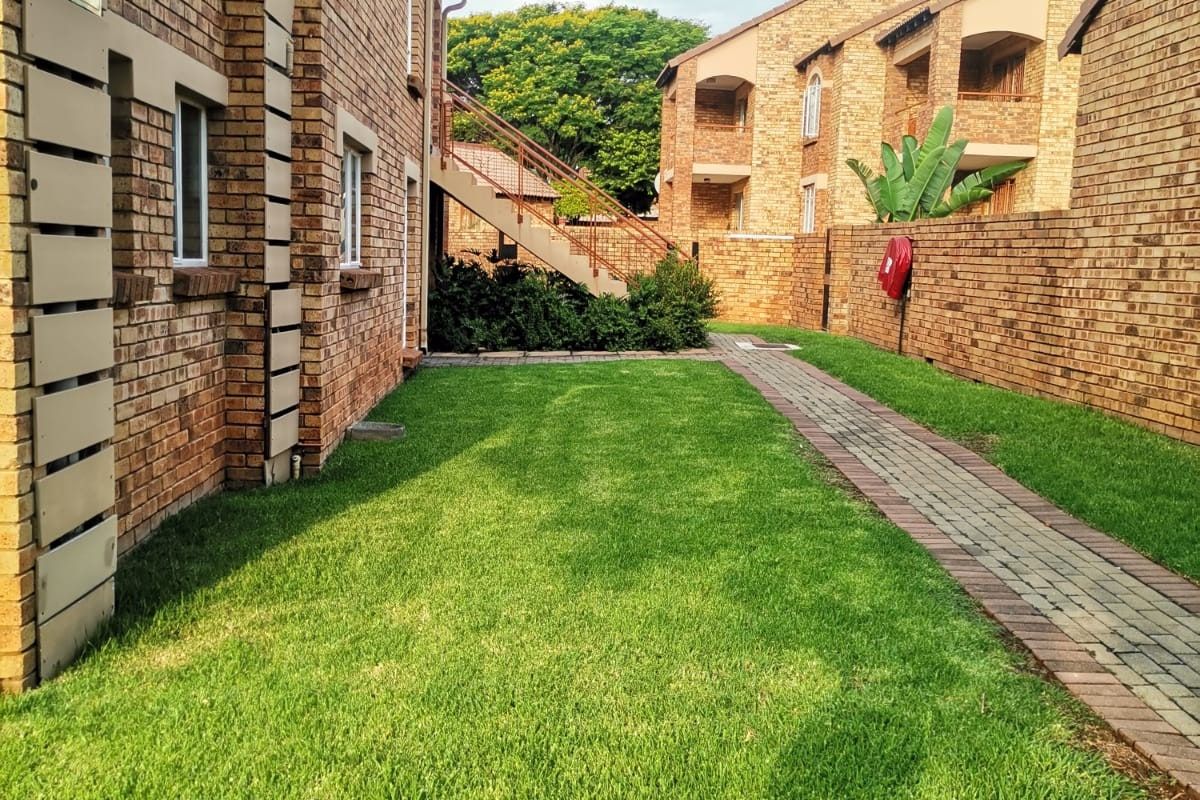 A well-maintained exterior rear view of the apartment complex featuring face brick architecture, a paved walkway, and a manicured lawn area.