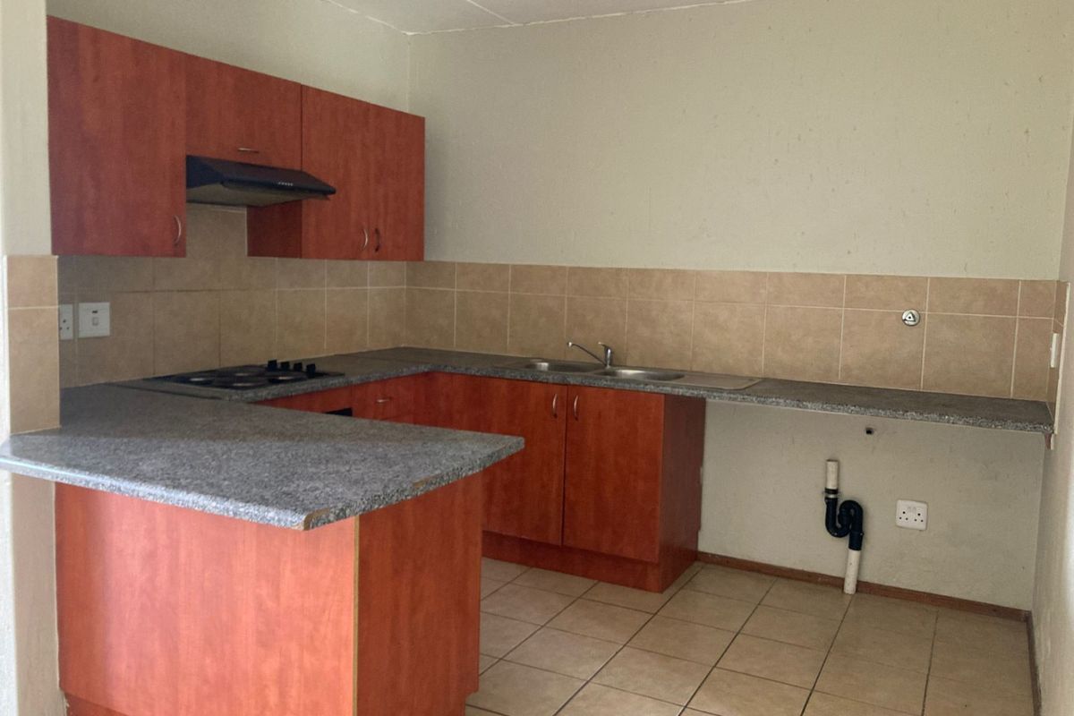 A functional kitchen featuring wood-look cabinetry, a built-in hob with extractor, and tiled flooring, offering a blank canvas for modern updates.
