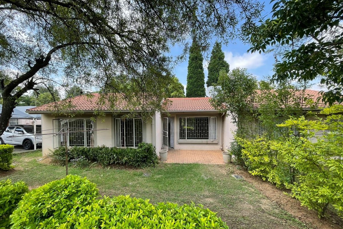 Rear view of the townhouse featuring a paved patio area, established garden, and tiled roof with security bars on the windows.