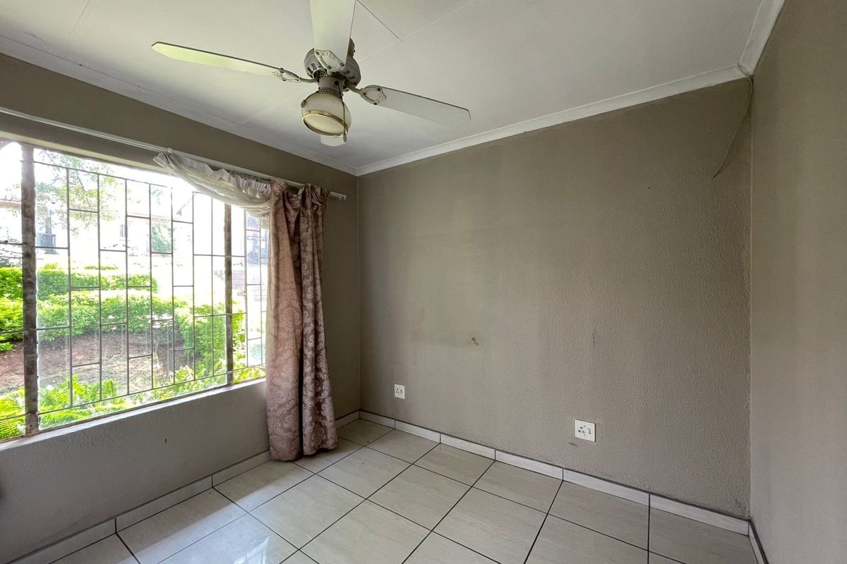 An empty bedroom featuring tiled flooring, a ceiling fan, and large windows fitted with security bars.