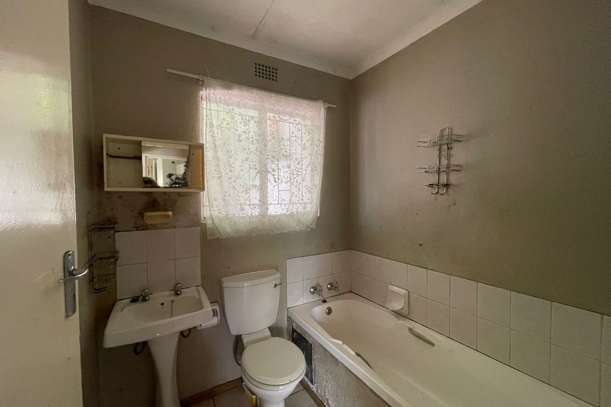 A dated bathroom featuring a pedestal basin, toilet, and bathtub with tiled splashbacks, requiring cosmetic updates and refurbishment of wall finishes.