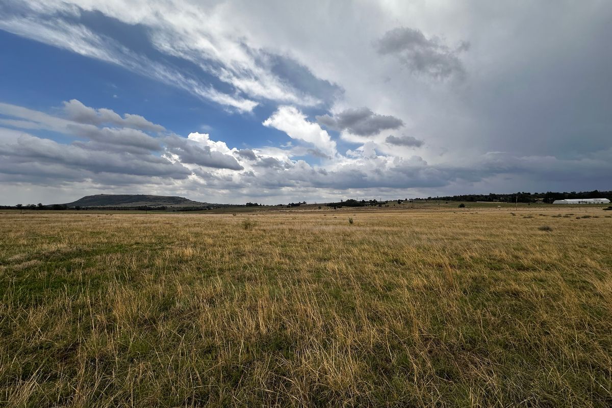 A wide-angle view of expansive, undeveloped grassland under a dramatic cloudy sky, showcasing the natural landscape of the property.
