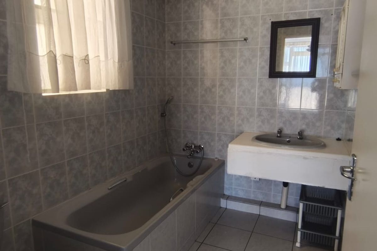 A dated bathroom featuring tiled walls, a built-in bathtub, and a wall-mounted basin, offering potential for a modern renovation.
