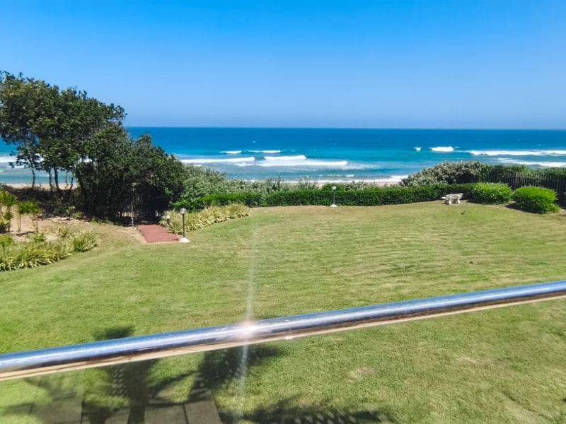 A scenic elevated view overlooking a lush green lawn and coastal landscape with a clear ocean horizon.