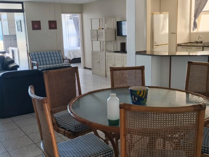 Open plan living and dining area featuring tiled floors, a functional kitchen with granite countertops, and sliding doors leading to a balcony with ocean views.