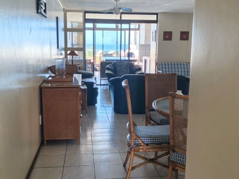 Open plan living and dining area featuring tiled flooring, a ceiling fan, and sliding glass doors leading to an outdoor balcony with ocean views.