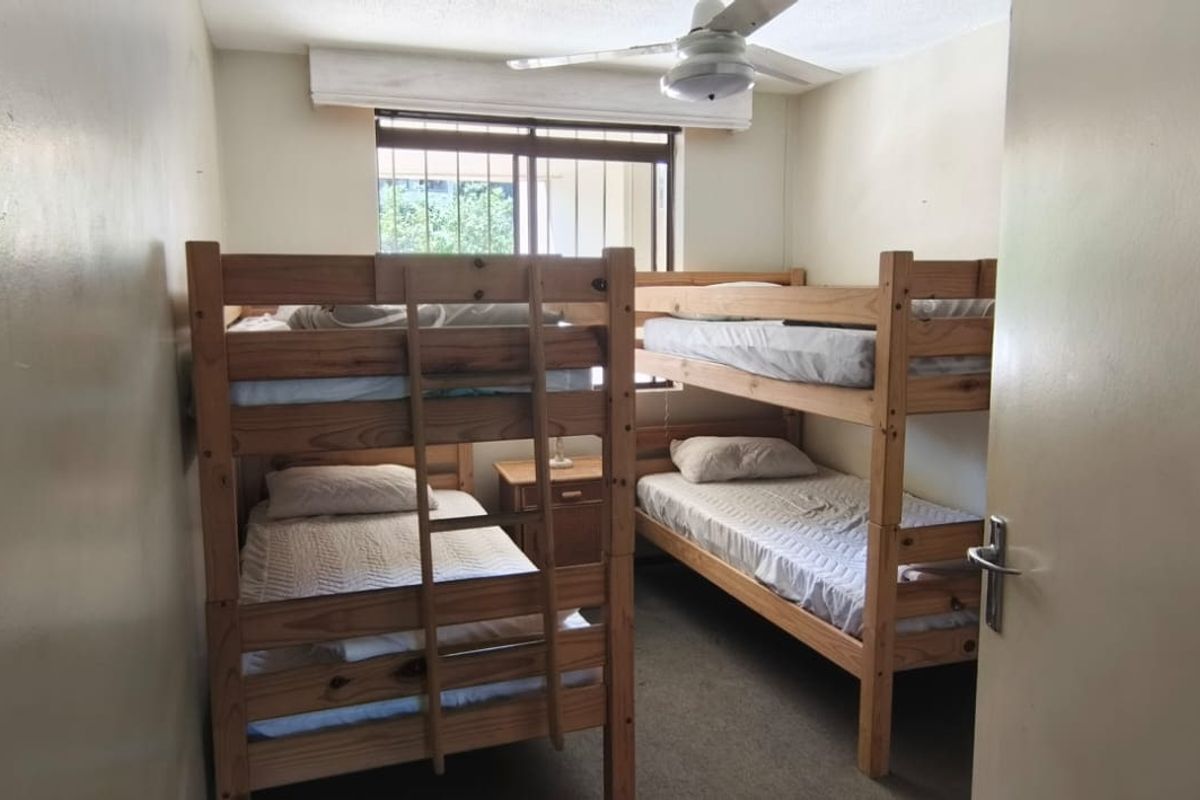 A compact bedroom featuring carpet flooring, a ceiling fan, and security bars on the window, currently configured with bunk beds.