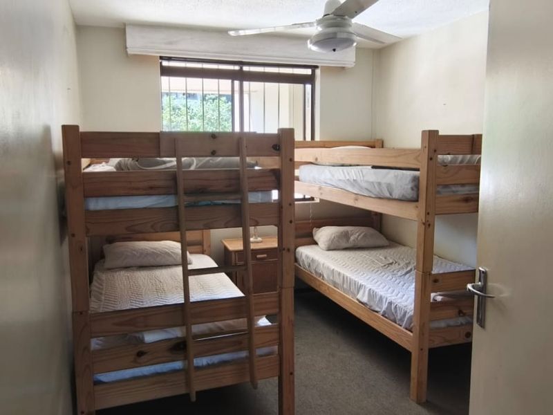 A compact bedroom featuring carpet flooring, a ceiling fan, and security bars on the window, currently configured with bunk beds.