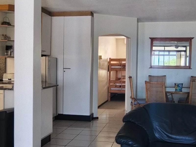 Open plan living area featuring a functional kitchen with built-in cabinetry and tiled flooring, leading to a dining space and adjacent bedroom access.