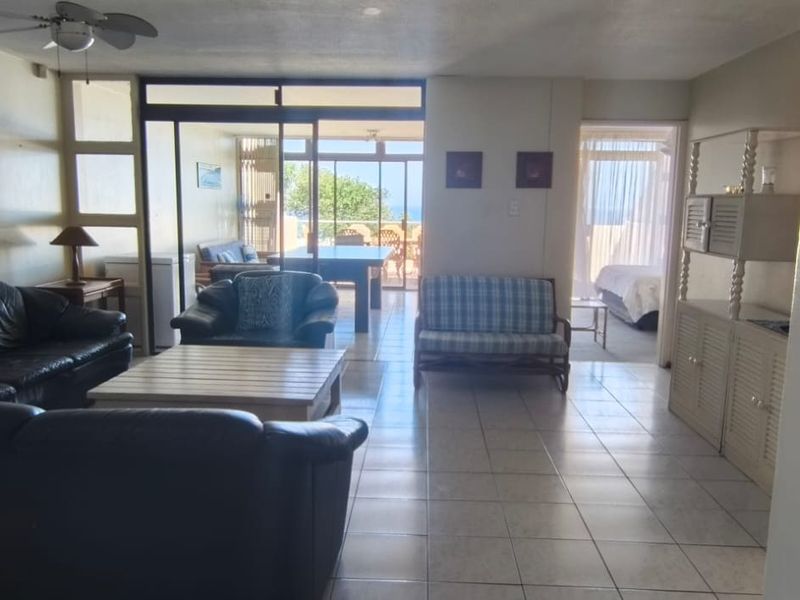 Spacious open-plan living area featuring tiled floors, ceiling fan, and large sliding glass doors leading to an outdoor balcony with ocean views.