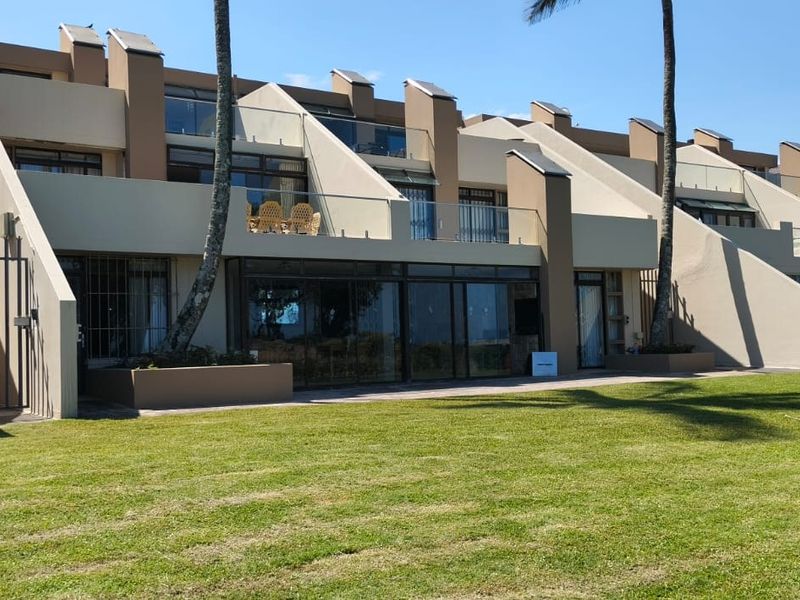 Rear view of a multi-level apartment complex featuring private balconies with glass balustrades, large sliding glass doors, and access to a shared lawn area.