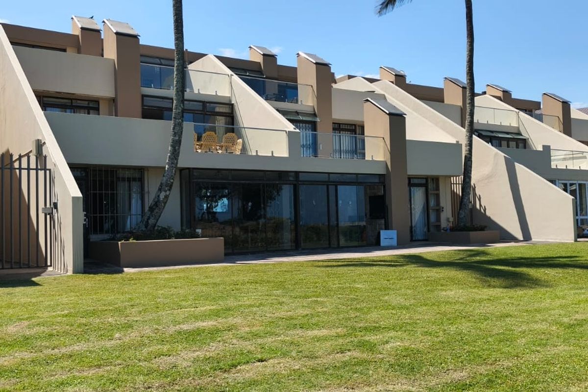Rear view of a multi-level apartment complex featuring private balconies with glass balustrades, large sliding glass doors, and access to a shared lawn area.