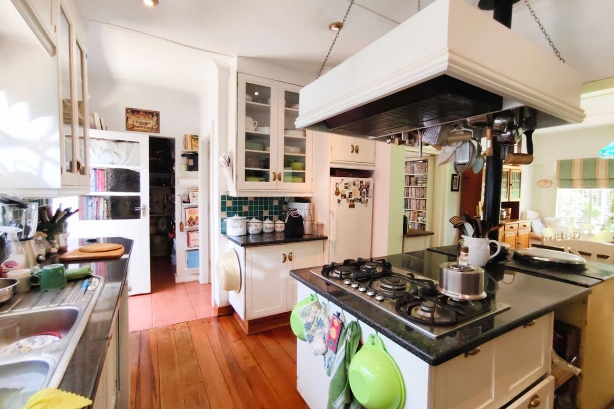 A functional kitchen featuring a central island with a gas hob, overhead extractor, granite countertops, and classic white cabinetry with hardwood flooring.