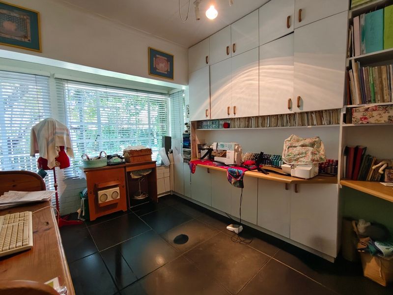 A functional home office or craft room featuring extensive built-in cabinetry, a dedicated desk area, and large windows with venetian blinds.
