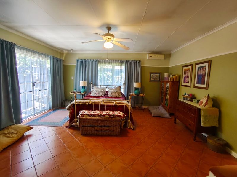 Spacious bedroom featuring terracotta floor tiles, a ceiling fan, split system air conditioning, and direct access to the outdoors via sliding glass doors.