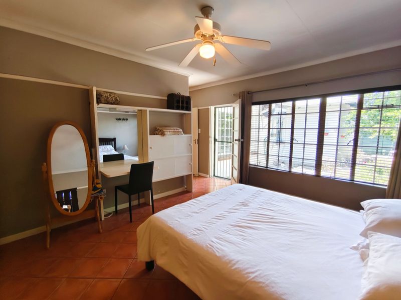 A bedroom featuring tiled flooring, a ceiling fan, built-in desk and shelving, and direct access to the exterior via a security gate.