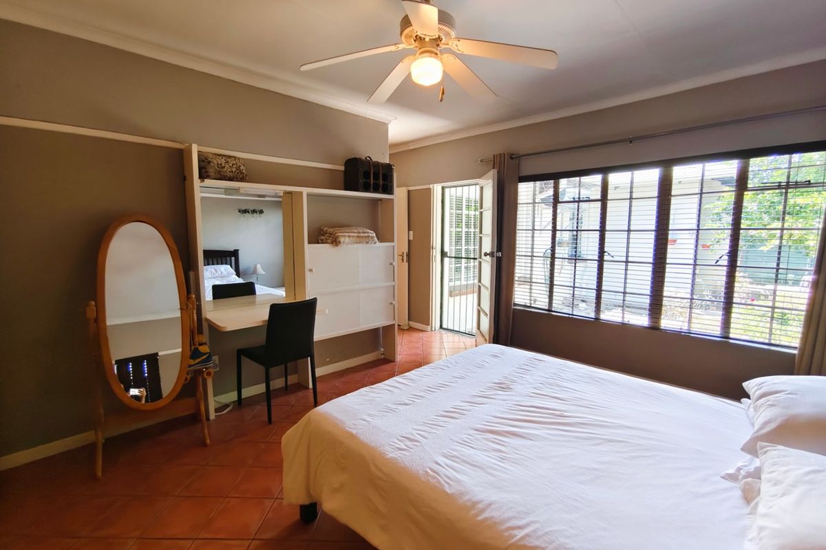 A bedroom featuring tiled flooring, a ceiling fan, built-in desk and shelving, and direct access to the exterior via a security gate.