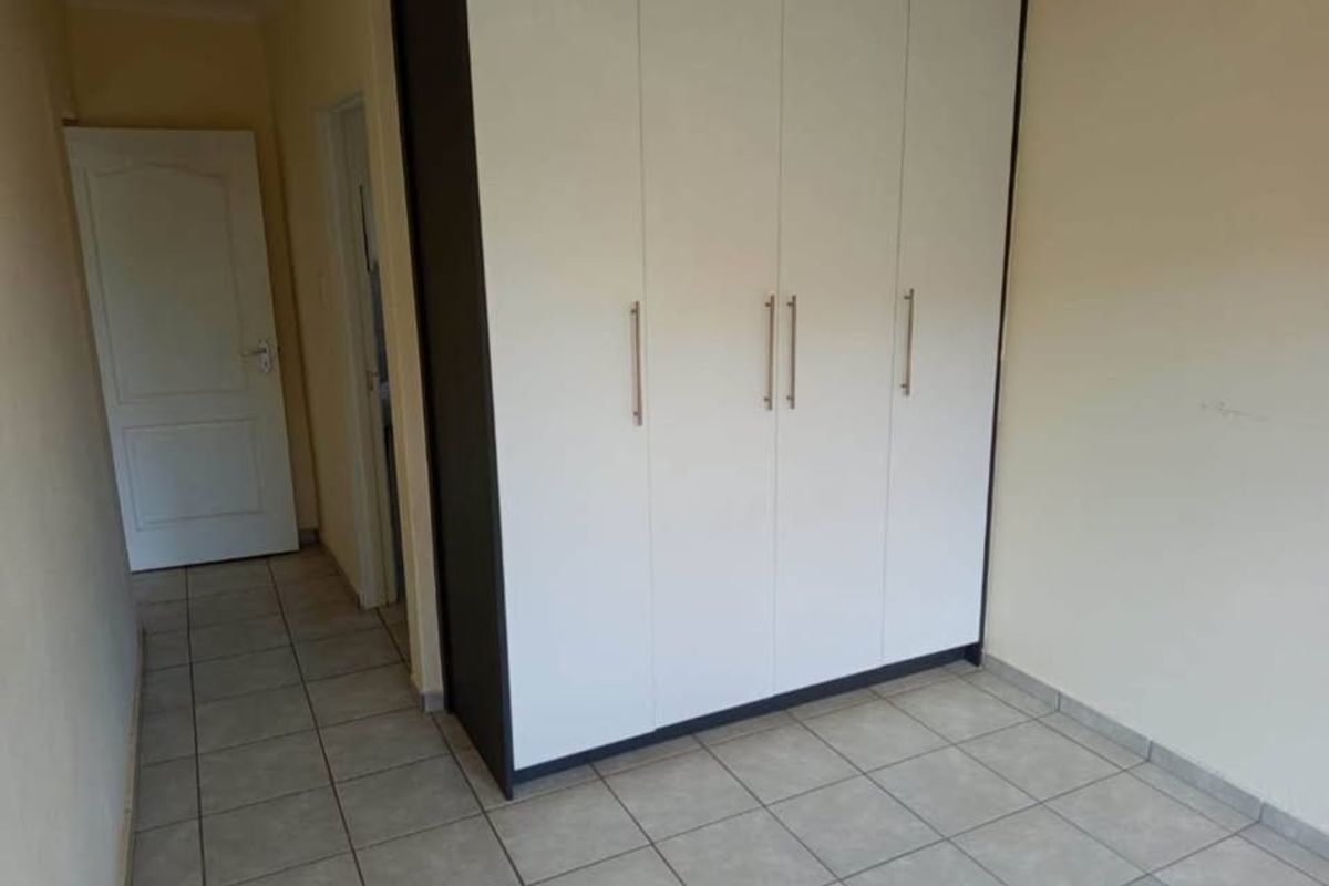 A clean, empty bedroom featuring neutral tiled flooring and a modern, white built-in wardrobe with dark framing.