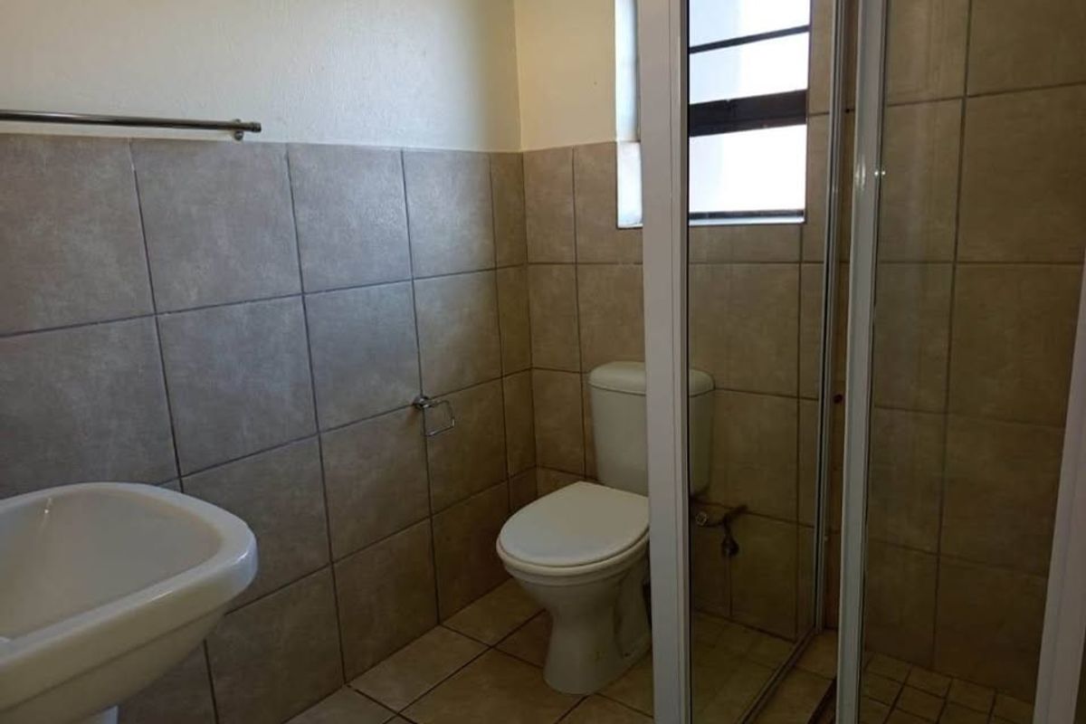 A functional bathroom featuring a pedestal basin, toilet, and a shower enclosure with tiled walls and flooring.