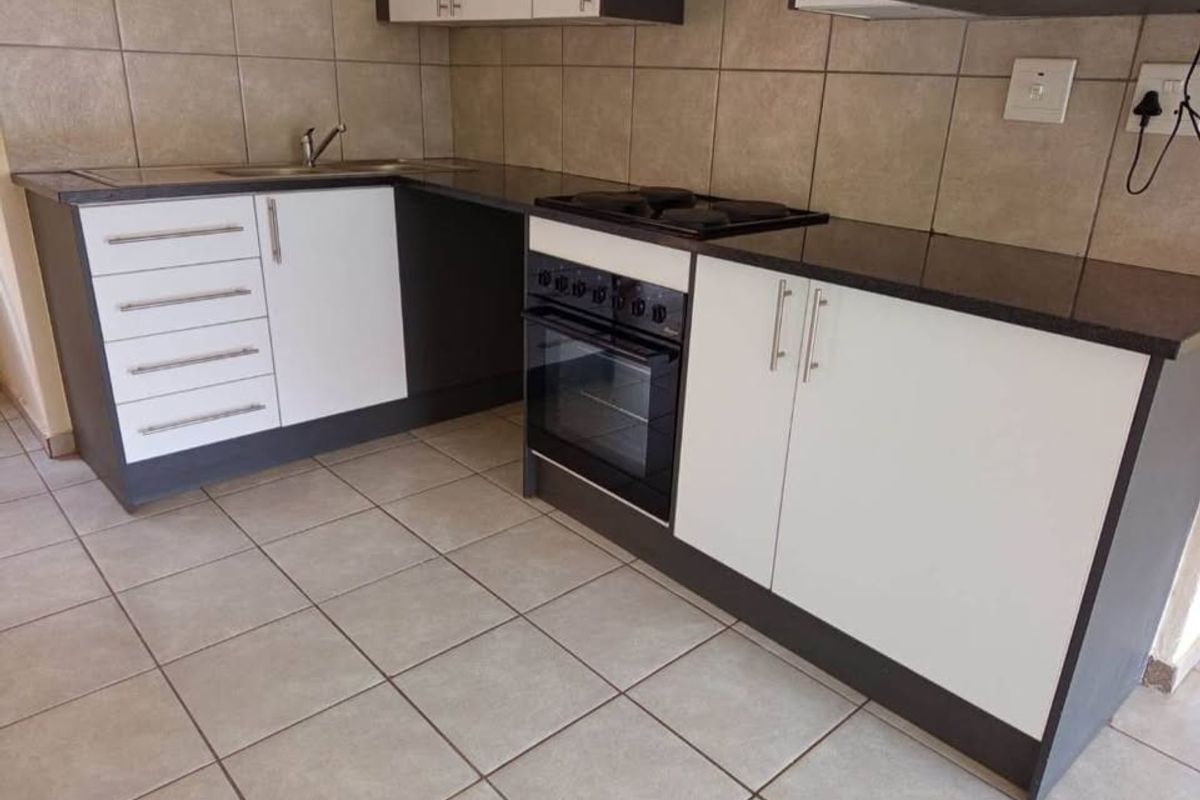 A functional kitchen featuring modern two-tone cabinetry, dark laminate countertops, a built-in oven with electric hob, and neutral tiled flooring and backsplash.