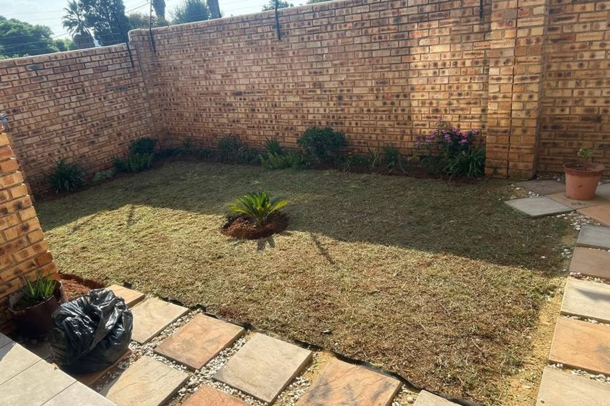 A private rear garden area featuring a brick boundary wall with electric fencing and a paved walkway leading to a small lawn.