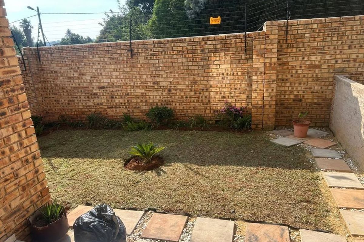 A private rear garden featuring a brick boundary wall with integrated electric fencing, paved walkway, and established lawn area.