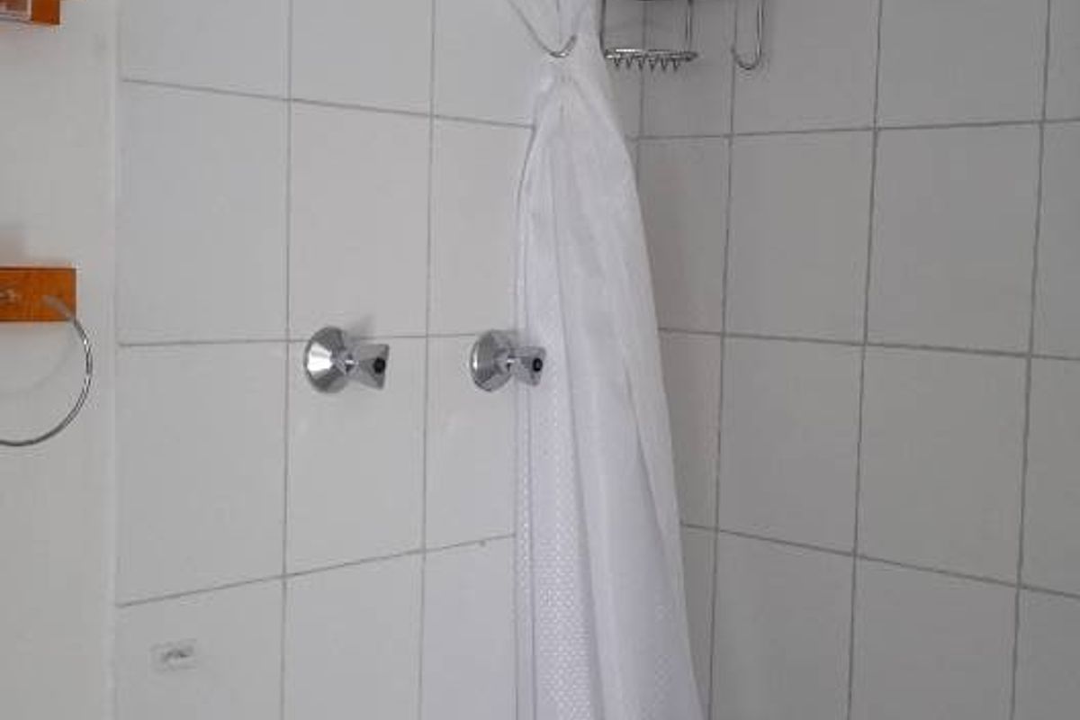 A functional shower enclosure featuring white wall tiles, a standard shower head, and tiled flooring.