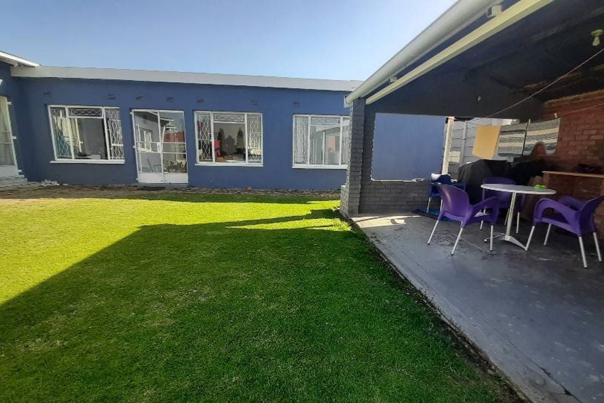 Rear view of the property featuring a lawn and a covered patio area with a built-in braai.