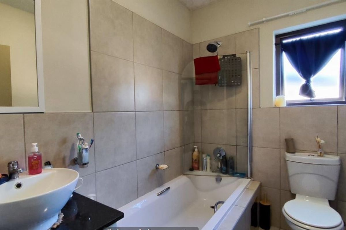 A functional bathroom featuring a bathtub with a glass screen, a vessel sink on a granite vanity, and neutral wall tiling.