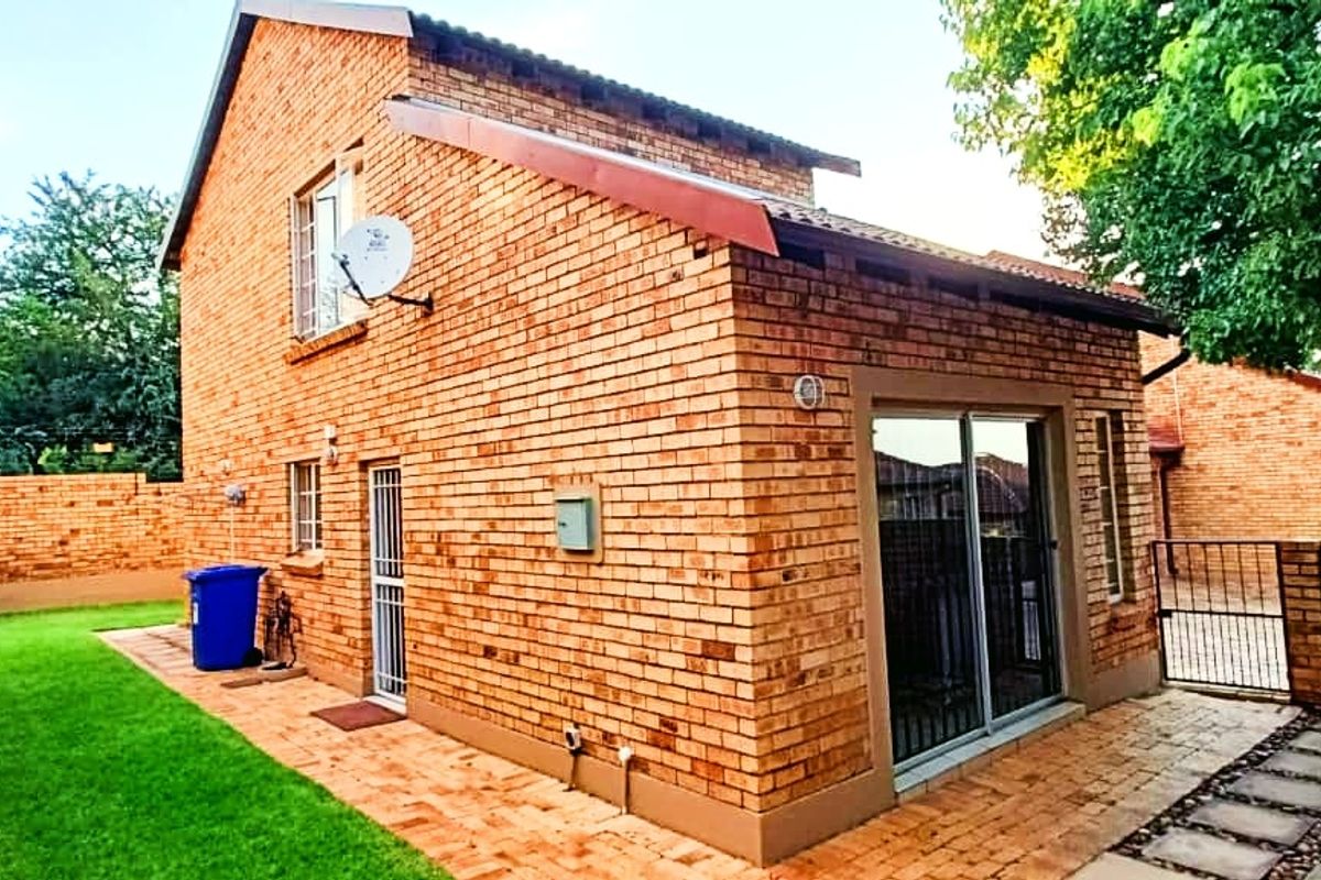 Rear view of a face brick townhouse featuring a paved patio area, small lawn, and secure sliding door access.