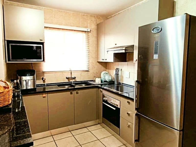 A functional kitchen featuring granite countertops, built-in oven, hob, extractor fan, and tiled finishes, offering a practical layout for daily meal preparation.