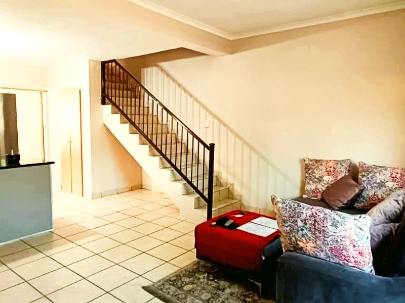 Open-plan living area featuring a tiled floor, staircase with metal balustrade, and a functional kitchen with island cabinetry.