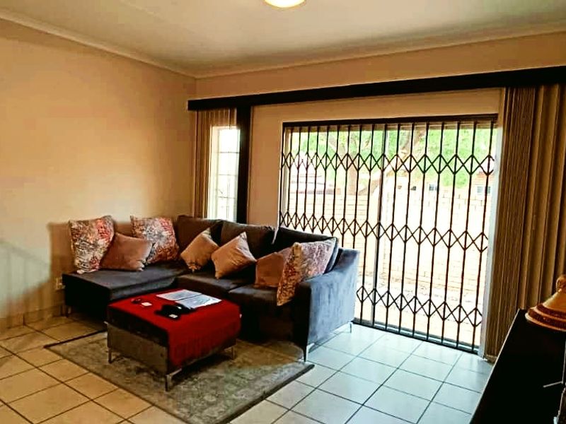 A living room featuring tiled flooring, a staircase with a metal railing, and a sliding door with a security gate leading to the exterior.