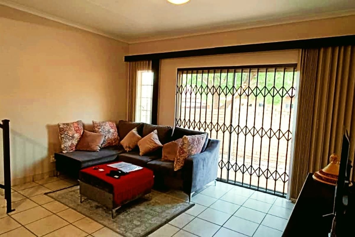 A living room featuring tiled flooring, a staircase with a metal railing, and a sliding door with a security gate leading to the exterior.